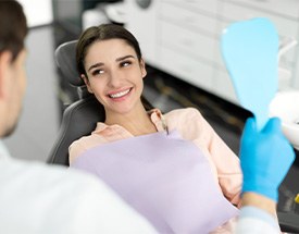 Woman smiling at dentist holding handheld mirror