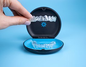 Two fingers holding Invisalign tray above its case with blue background