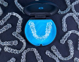 Bird’s eye view of numerous aligners around an Invisalign case on a black surface