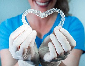 Tech in blue scrubs and white gloves holding Invisalign in heart shape