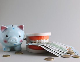 Blue spotted piggy bank next to artificial teeth holding $100 bills and scattered coins